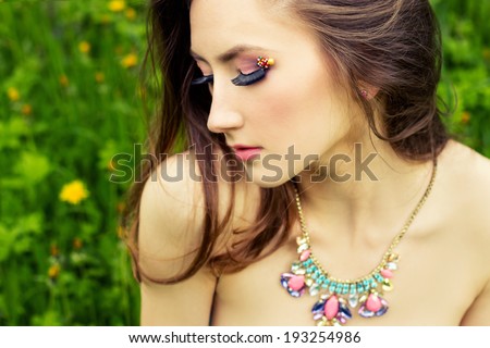 beautiful young girl with long hair and beautiful makeup with necklace on the neck sitting on the grass in the garden