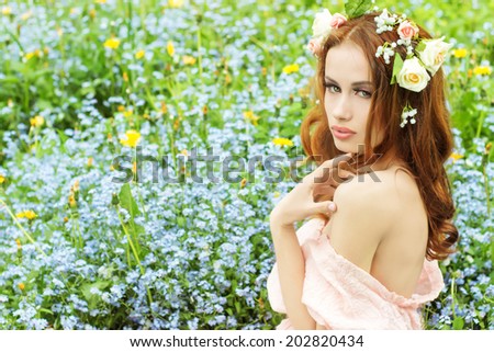 beautiful sexy young girl with long red hair with flowers in her hair, sitting in a field in blue flowers