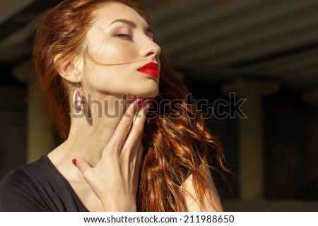 beautiful sexy girl with red hair with big red lips with makeup in the city on a Sunny summer day
