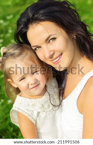 happy family, mother and daughter dressed in white sitting on the grass in a Park on a Sunny summer day