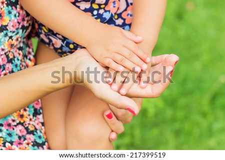 Hands of mother and daughter holding each other. Summer park in background