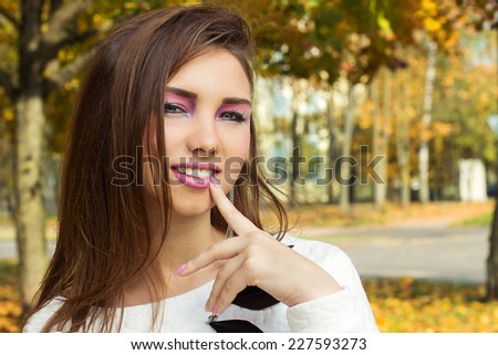 beautiful happy smiling girl with bright makeup in rock style with plump lips with a finger to her mouth in the Park warm autumn day