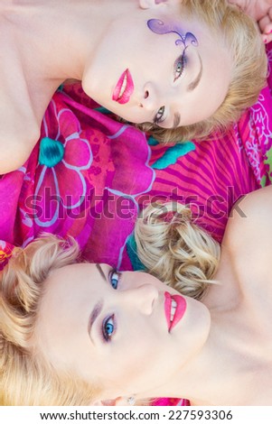 beautiful sexy girls, sisters with bright makeup and red lips lie on a bright blanket in a Park on a warm summer day