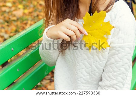 beautiful girl in a white jacket and black pants with yellow leaves in the hands of sitting on the bench in autumn Park