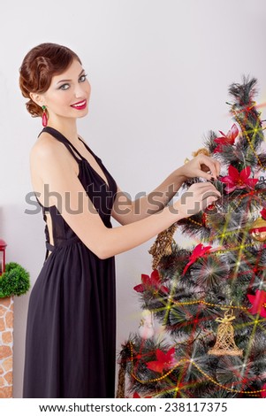 beautiful sexy happy smiling young woman in evening dress with bright makeup with red lipstick, decorates a Christmas tree for the new year