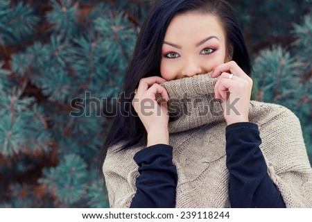 beautiful young happy woman winter day in the forest near trees hides his face under jacket