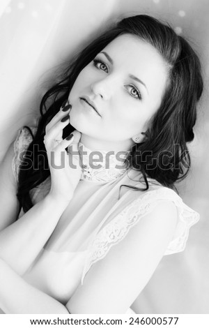 black and white photo beautiful girl with long dark hair in a white bodysuit behind the curtain near the window