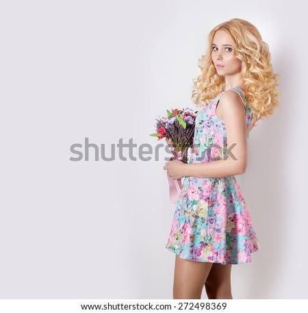beautiful sexy modest sweet tender girl with curly blond hair standing on white background with a bouquet of flowers of lavender in blue summer dress
