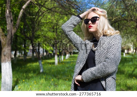 beautiful sexy blonde woman in sunglasses and a coat to go to the apple orchard on a sunny spring day