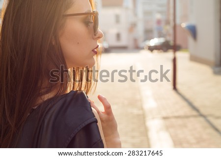 beautiful stylish girl in a black leather jacket with sunglasses with a dark lipstick in the city at sunset