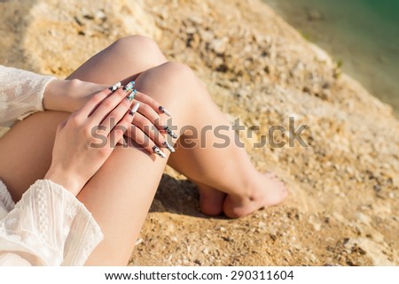 beautiful long legs on the shore of the blue lake , lie the hands on the knees with long acrylic nails