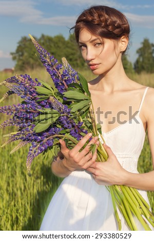 beautiful sexy woman in white sundress with a bouquet in the hands of lupine in field at sunset
