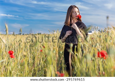beautiful sexy cute girl with big lips and red lipstick in a black jacket with a flower poppy standing in a poppy field at sunset on a sunny warm summer day