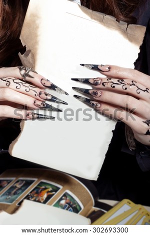 beautiful hands with long acrylic witch black nails holding a white sheet in the hands of