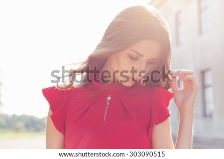beautiful sexy girl in a red dress with a gentle look into the sun at sunset in bright sunny day