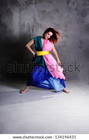 Young modern dancing girl in colorful dress on the dirty grunge grey studio background