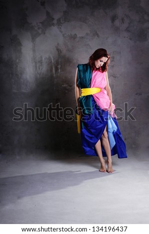 Young modern dancing girl in colorful dress on the dirty grunge grey studio background