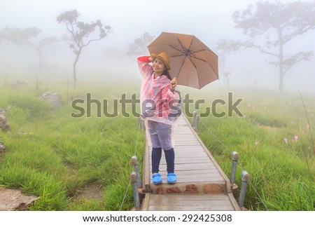 Asian woman under umbrella view Tree and flower Wild siam tulip blooming of forest on Morning Mist at Tropical Mountain Range after rain fall at PaHinNgam National Park, Chaiyaphum Province, Thailand
