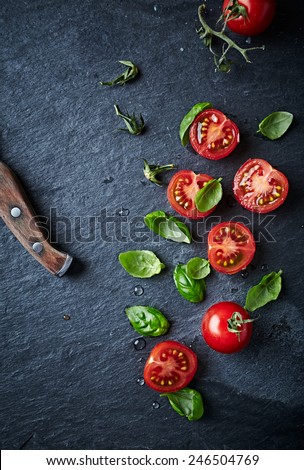 Halved cherry tomatoes and basil leaves on black slate