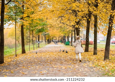 beautiful little girl runs for birds in autumn park