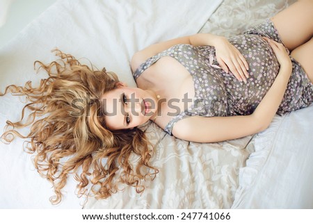 young pregnant woman smiling lying on the bed and touching belly