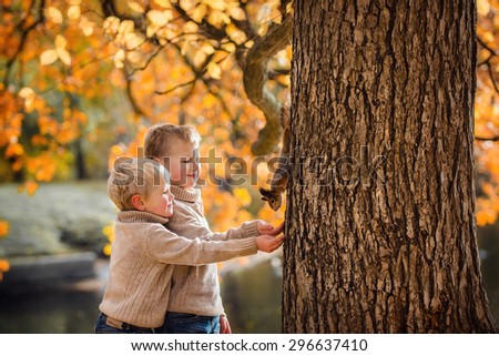 Happy kids feeds a little squirrel in autumn park