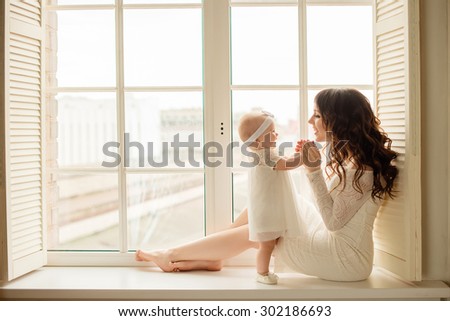 Loving mother playing with her baby sitting on a window