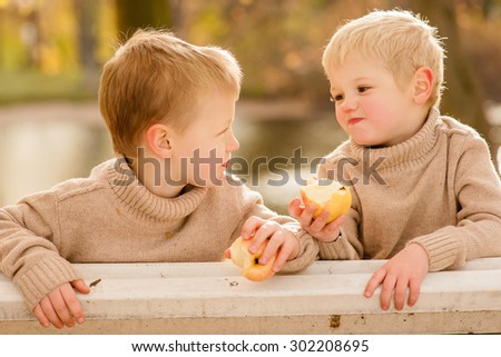 little boys eats an apple sitting on a bench in the autumn park