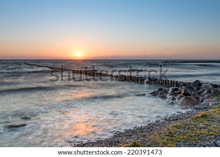 Rocks and wooden wave  breaker poles in the sea surf in the sunset