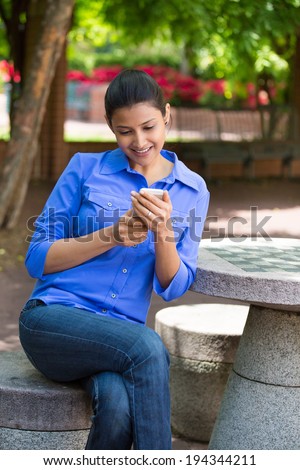 Closeup portrait, young happy business woman sitting, checking her cellphone, isolated on background of a park, trees and flowers, on a sunny summer day. Business communication