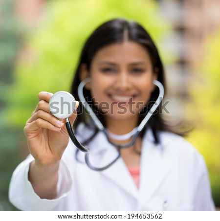 Closeup portrait of female, health care professional or doctor or nurse holding up stethoscope, isolated background of blurred trees and buildings