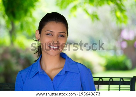 Closeup headshot portrait young beautiful happy business woman in blue shirt, sitting on bench, isolated green trees, nature background. Positive human emotion facial expression feelings
