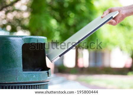 Closeup cropped portrait of someone tossing old notebook computer in trash can, isolated outdoors green trees background