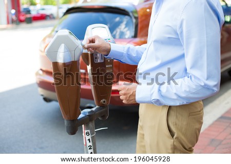 Closeup portrait, young man putting coins in parking meter outside to prevent fines, isolated roads, car, trees background.