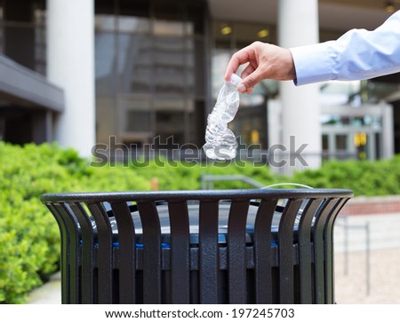 Closeup portrait, hand throwing plastic empty water bottle in recycling bin, isolated building and trees background