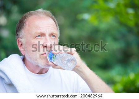 Closeup portrait, thirsty senior mature man drinking water outside, isolated green tree foliage background