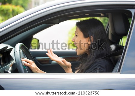 Closeup portrait, angry young sitting woman pissed off by drivers in front of her and gesturing with hands, isolated city street background. Road rage traffic jam concept.