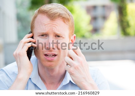 Closeup portrait, worried young man in blue shirt talking on phone to someone, looking gloomy, isolated outdoors outside background