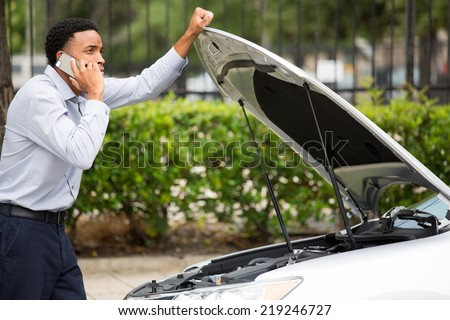 Closeup portrait, young man having trouble with his broken car, opening hood and calling for help on cell phone, isolated green trees outside background