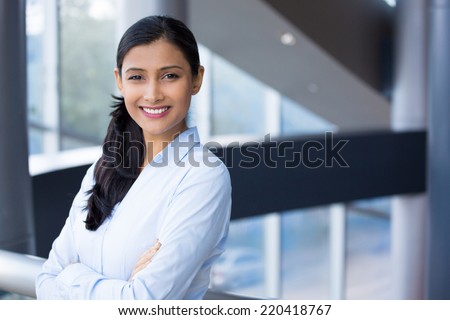 Closeup portrait, young professional, beautiful confident woman in blue shirt, arms crossed folded, smiling isolated indoors office background. Positive human emotions