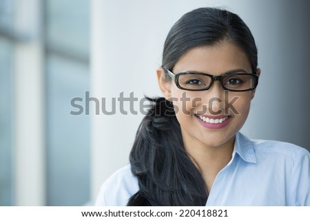 Closeup portrait, young professional, beautiful confident adult woman in blue shirt, with black glasses, smiling isolated indoors office background. Positive human emotions
