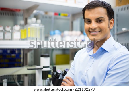 Closeup portrait, young friendly scientist standing by microscope. Isolated lab background. Research and development sector