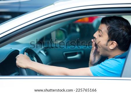 Closeup portrait tired young funny man in blue shirt with short attention span, driving his black car after long hours trip, yawning at wheel, isolated outside background. Sleep deprivation