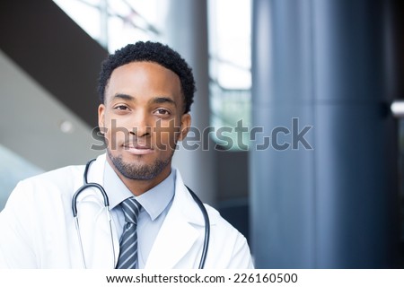 Closeup portrait head shot of friendly, smiling confident male doctor, healthcare professional with a white coat and stethoscope, looking at the camera, isolated hospital clinic background.