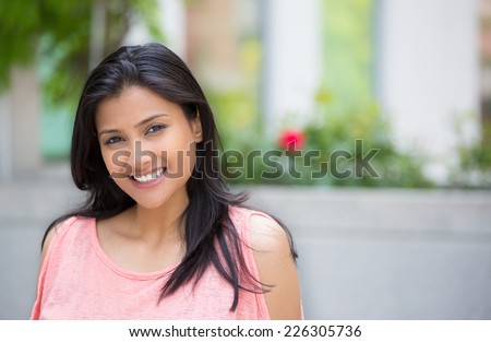 Closeup portrait of confident smiling happy pretty young woman in pink dress, isolated background of blurred trees, flowers. Positive human emotion facial expression feelings, attitude, perception