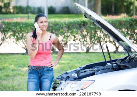 Closeup portrait, young woman in pink tanktop having trouble with her broken car, opening hood and calling for help on cell phone, isolated green trees and shrubs outside background