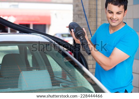 Closeup portrait, young man driver in blue shirt, air drying his silver car with vacuum hose after washing. Safe for expensive paint and chrome. A touch less process that keeps the wax intact