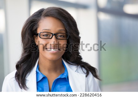 Closeup headshot portrait of friendly, smiling confident female healthcare professional with lab coat and black glasses. Isolated hospital clinic background. Time for an office visit
