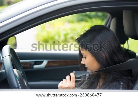 Closeup portrait young serious, attractive woman pulling on seatbelt inside black car. Driving safety, buckle up to prevent traffic death from accidents concept. Life-saving measures