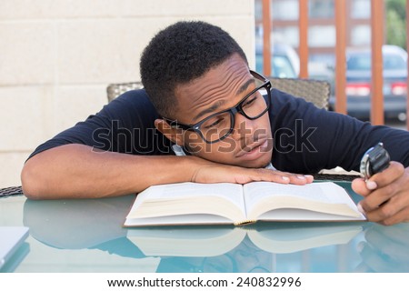 Closeup portrait, nerdy young man in big black glasses holding watch, falling very tired of reading, isolated outdoors outside background. The clock is ticking, can't focus